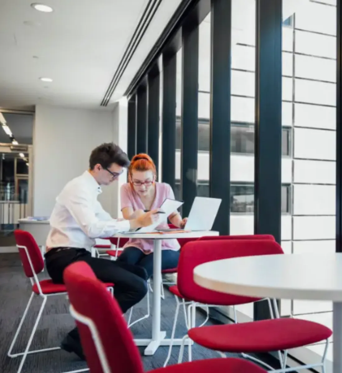 Two office workers collaborating at a desk by the window